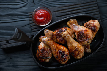 Grilled chicken legs with sauce on a black wooden background