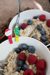 Oatmeal with berries in a bowls. Rasberries and blueberries. Flax seeds. Christmas style clips. Santa Claus and Christmas tree