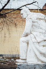 Damaged Lenin statue sitting on a chair with  book in his hand.