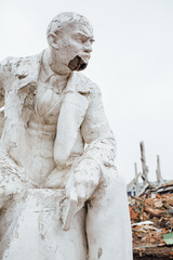 Damaged Lenin statue sitting on a chair with  book in his hand.