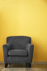 Comfortable grey armchair on yellow wall background