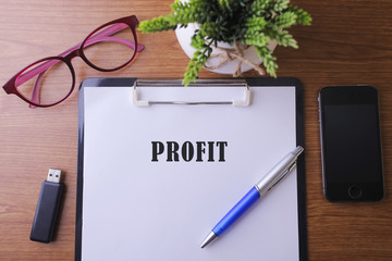 Office desk with a paper written PROFIT with pen, glass, smartphone