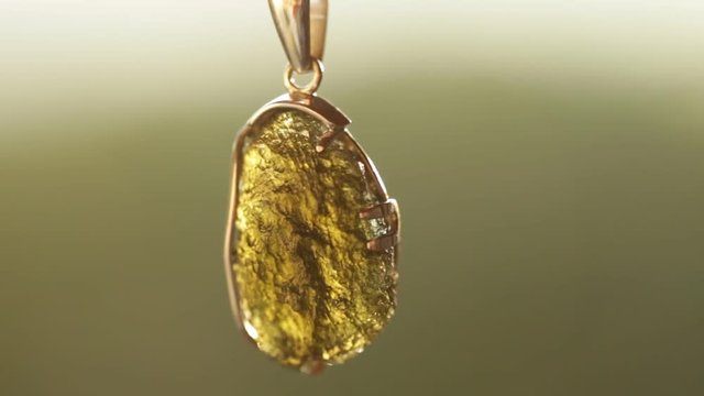 woman's hand and a silver pendant with a stone vltavin on blurred background