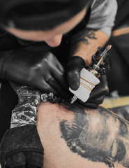 Tattoo master in black gloves, tattoo on the skin of black ink tattoo of his client in the salon.