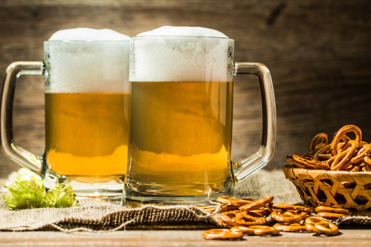 Two beer mugs with hops and pretzels on linen cloth