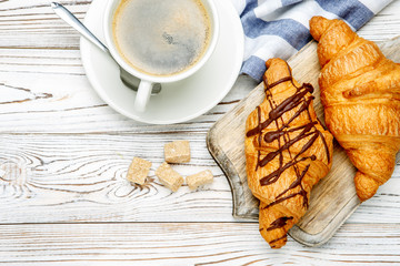 two fresh croissants and coffee on wooden background