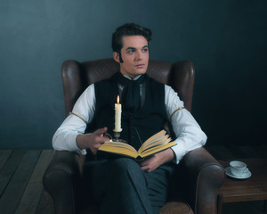 Retro victorian dickens style man reading book by candlelight.