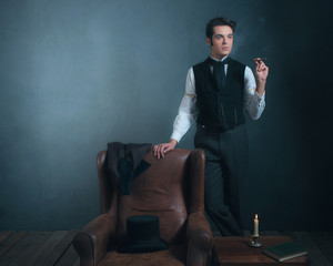 Vintage victorian man standing next to chair smoking cigarette.
