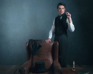 Vintage victorian man standing next to chair smoking cigarette.