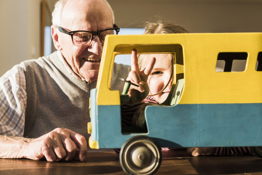 Grandfather and granddaughter assembling toy bus, girl making victory sign