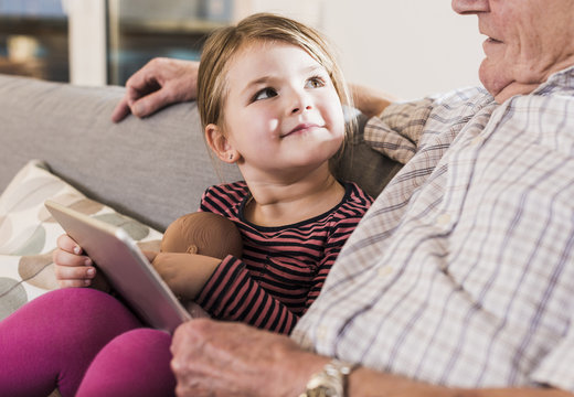 Grandfather reading out story for his granddaughter, using ebook