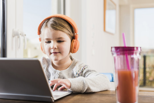 Little girl sitting at home using laptop and headphones