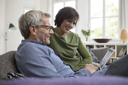 Smiling mature couple at home on the sofa sharing tablet
