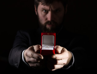 bearded man in business suit gives a ring in the red box and expresses different emotions on dark background