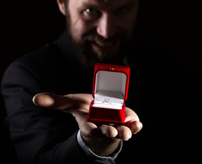 bearded man in business suit gives a ring in the red box and expresses different emotions on dark background