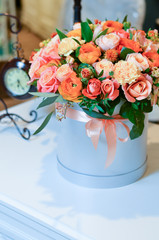 Букет из розовых и бежевых роз в серой шляпной коробке на столе рядом со старинными часами