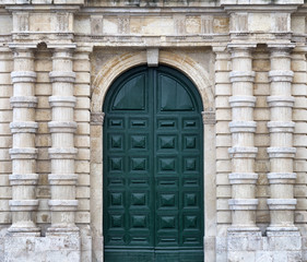 Detail of an old urban building stone facade with tall green wood door and decorative columns, Valletta, Malta