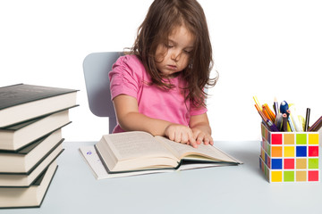 Small girl in pink t-shirt learning how to read at her desk