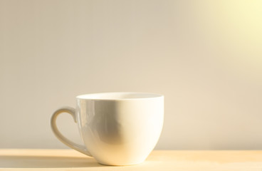 White coffee cup placed on a wooden floor with a white background and soft light