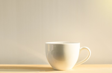 White coffee cup placed on a wooden floor with a white background and soft light