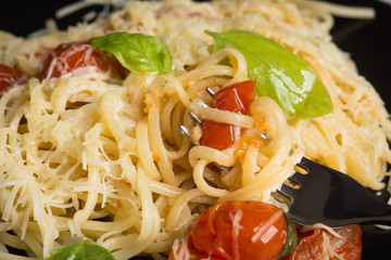 Pasta with tomatoes and basil on the dark background. Shallow depth of field.