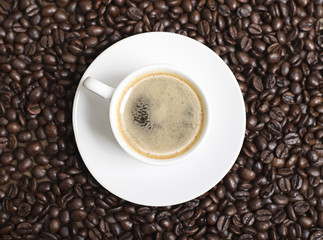 Close-up view from above of a cup of coffee over coffee beans. Texture.