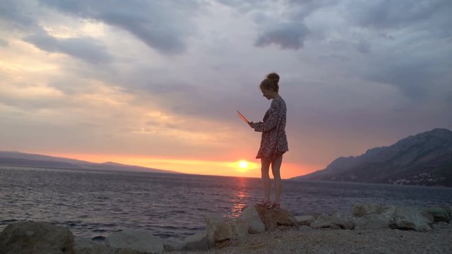 Girl working with her laptop computer near the sea at sunset in summer windy day. young woman using laptop in holiday