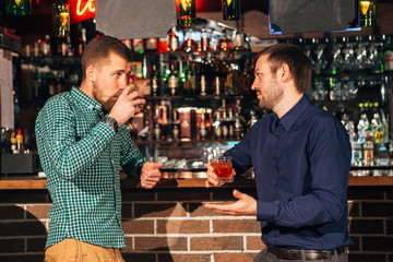 two young man talking at counter.  friends standing in bar and drinking whisky