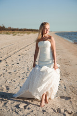 Fototapeta na wymiar Bride walking along sea coast wearing beautiful wedding dress