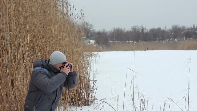 Young photographer makes the photo on the pond ice. He breathes his arms trying to keep warm.