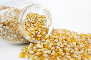 Yellow popcorn kernels spilling from jar. 