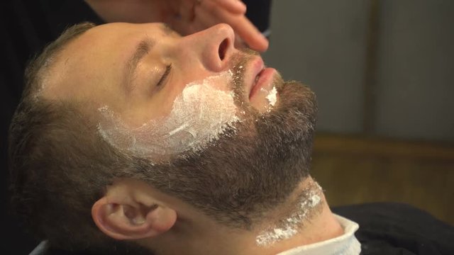 Barberman using soft cream on face of man with beard