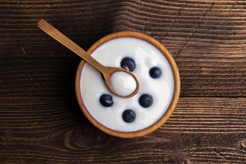 White yogurt in natural wooden bowl with blueberries. Top view on rustic background.