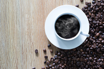 White coffee cup and pile of coffee seeds on brown wooden plate / top view and select focus