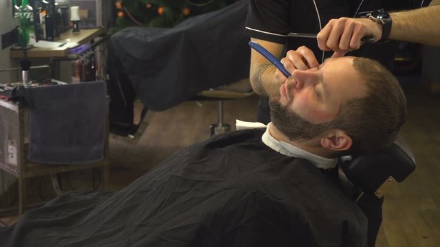 Barberman shaving beard of man