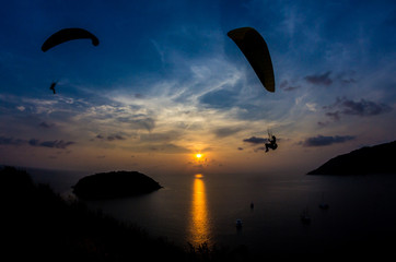 Silhouettes of paragliders flying in a sunset at Promthep Cape, Phuket, Thailand.