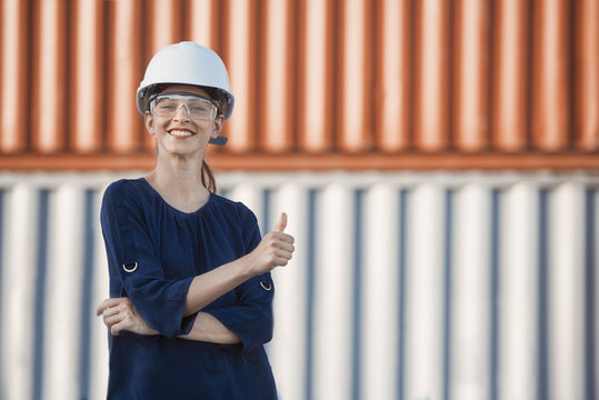 smiling woman, a logistics engineer is giving thumbs up in front of cargo containers