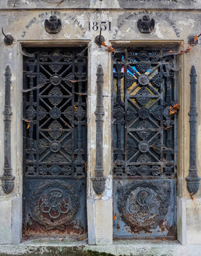 Twin door - two rusty blue rectangular ornate steel doors. Seperate decaying entrances to an abandoned tomb / crypt at a graveyard. Iron ornaments of flowers, faces and eagles, Latin inscriptions.