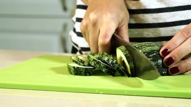 Cooking ratatouille. Female hands cutting zucchini into slices on plastic cutting board. HD