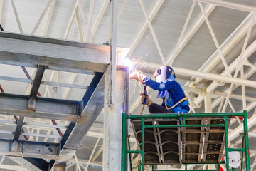 worker in protective glasses welding for fixing steel construction frames at construction building site