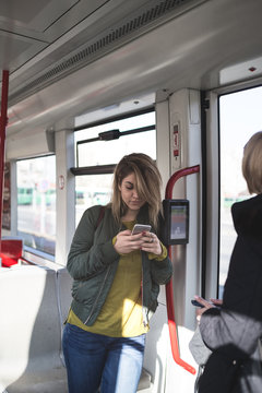 Beautiful young woman standing in tram and doing something on her cell phone. 