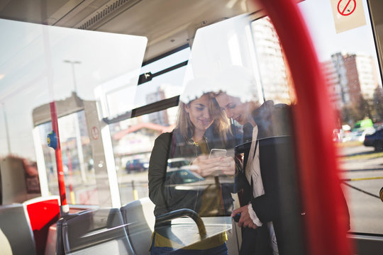Two beautiful young women standing in tram and talking. Photo is captured from outside through window glass.