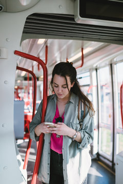 Beautiful young woman standing in tram and doing something on her cell phone. 