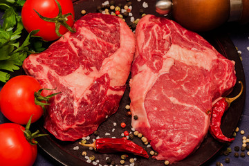 Still life from Raw beef steak with tomatoes, parsley and spices on black background, top view
