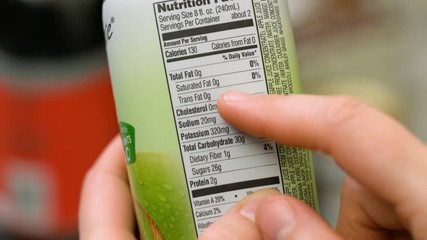 Grocery shopper reading nutrition label on a bottle of fruit juice at grocery store. 