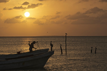 Fototapeta premium Setting sun on water with silhouette of fisherman