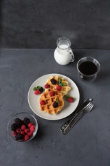 Whole wheat breakfast waffle served with blackberries, raspberries and mint leaves. Copy space on the grey stone background.
