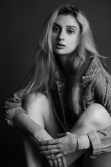 black and white portrait of a beautiful sad blonde girl in a denim jacket. girl sits with folded hands