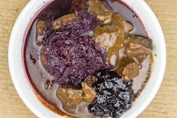 Overhead view of plate of cooked meat in gravy with cabbage on wooden table