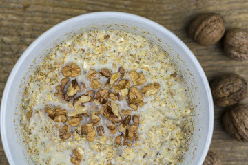 Overhead view of bowl of porridge with healthy whole walnuts on wooden table